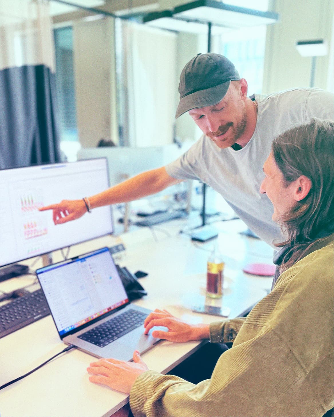 two working people in an office, one is pointing at a screen